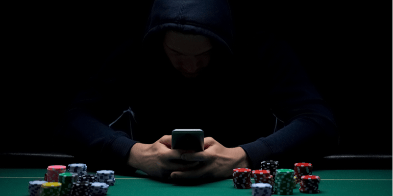 暗闇の中で携帯と触る手とサイコロがカジノ台に置かれている画像